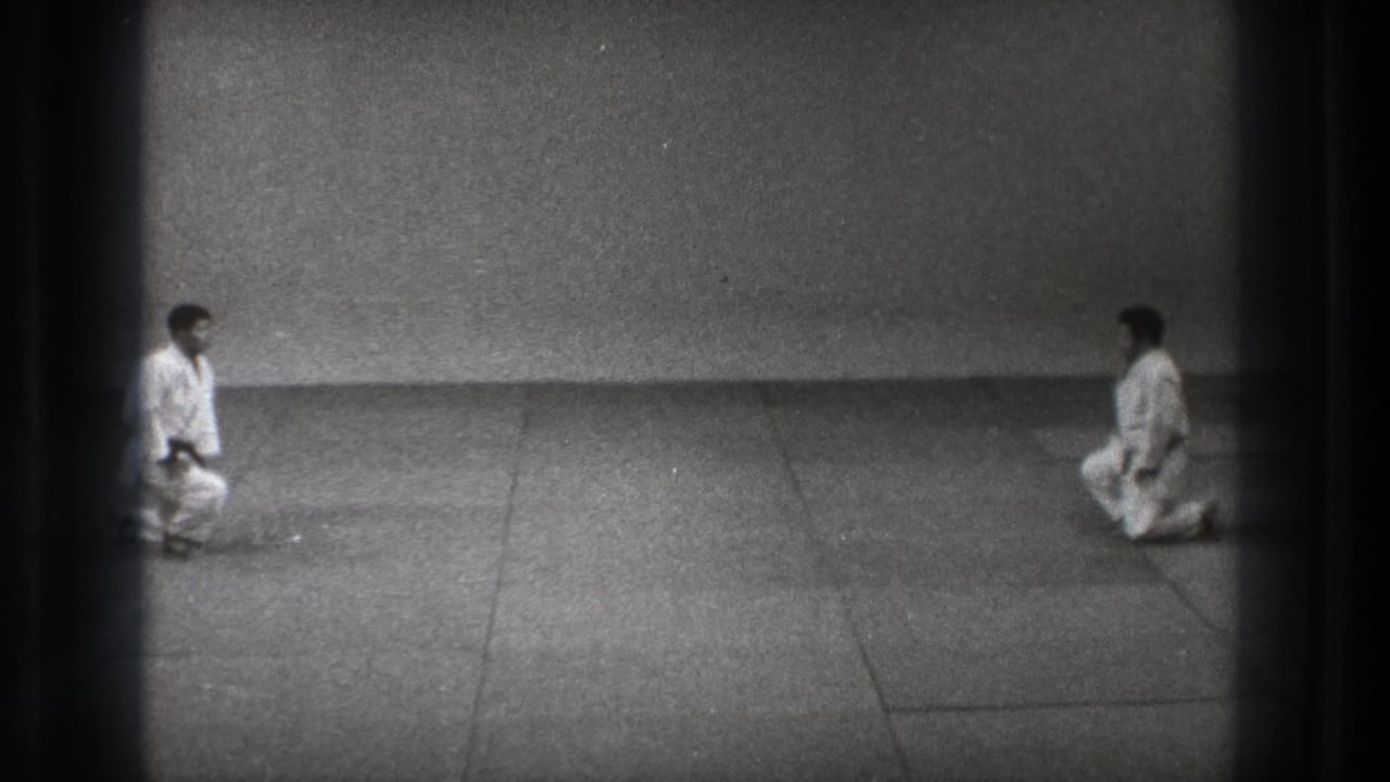 Two karate practitioners in white uniforms kneel across from each other in the 1971 Tokyo home-movie scene.