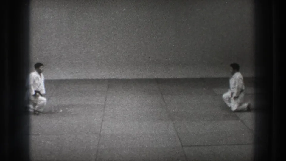 Two karate practitioners in white uniforms kneel across from each other in the 1971 Tokyo home-movie scene.