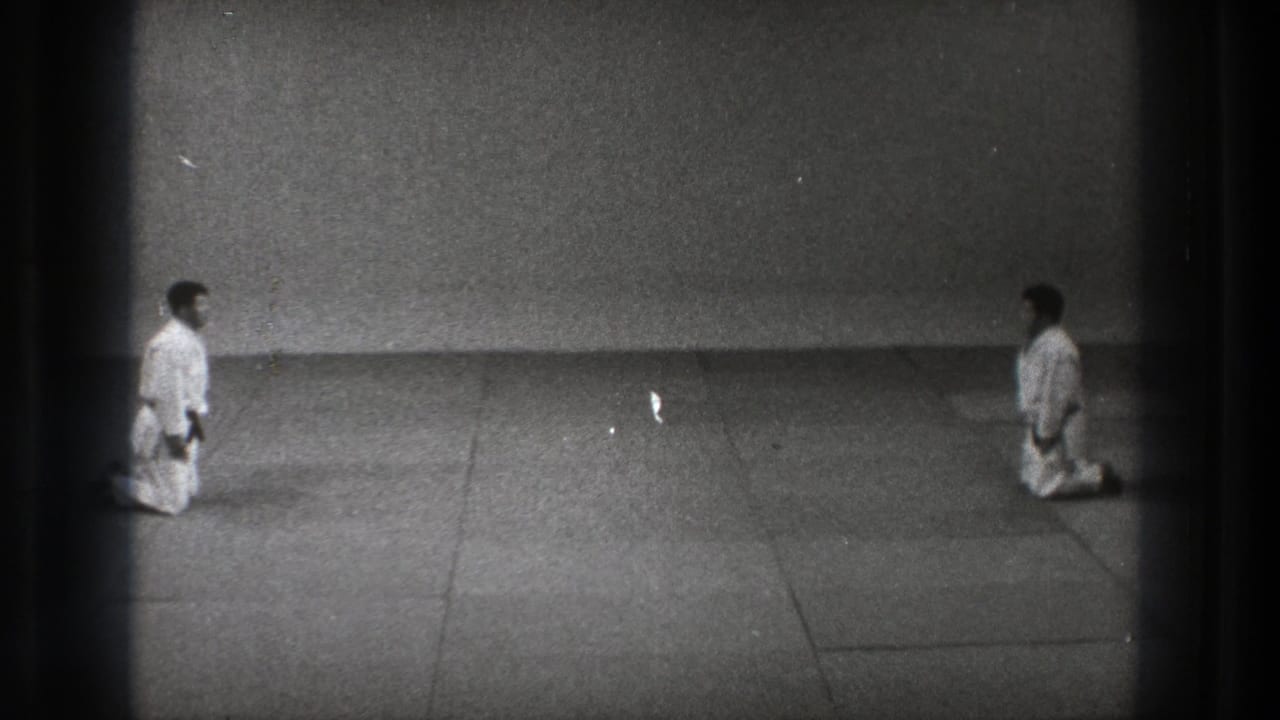 The 8mm frame shows two martial artists kneeling in white uniforms, facing one another across a plain mat in Tokyo.