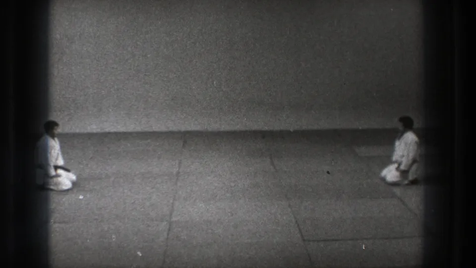 Two karate practitioners remain kneeling at opposite ends of the mat in grainy 1971 Tokyo 8mm footage.