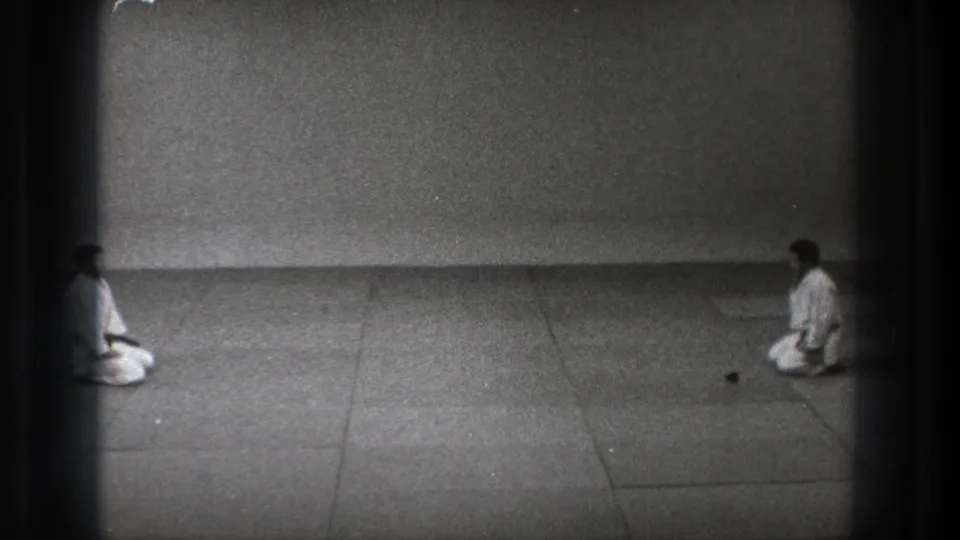 1971 Tokyo 8mm frame showing two martial arts practitioners kneeling across a matted dojo floor before a formal bow.