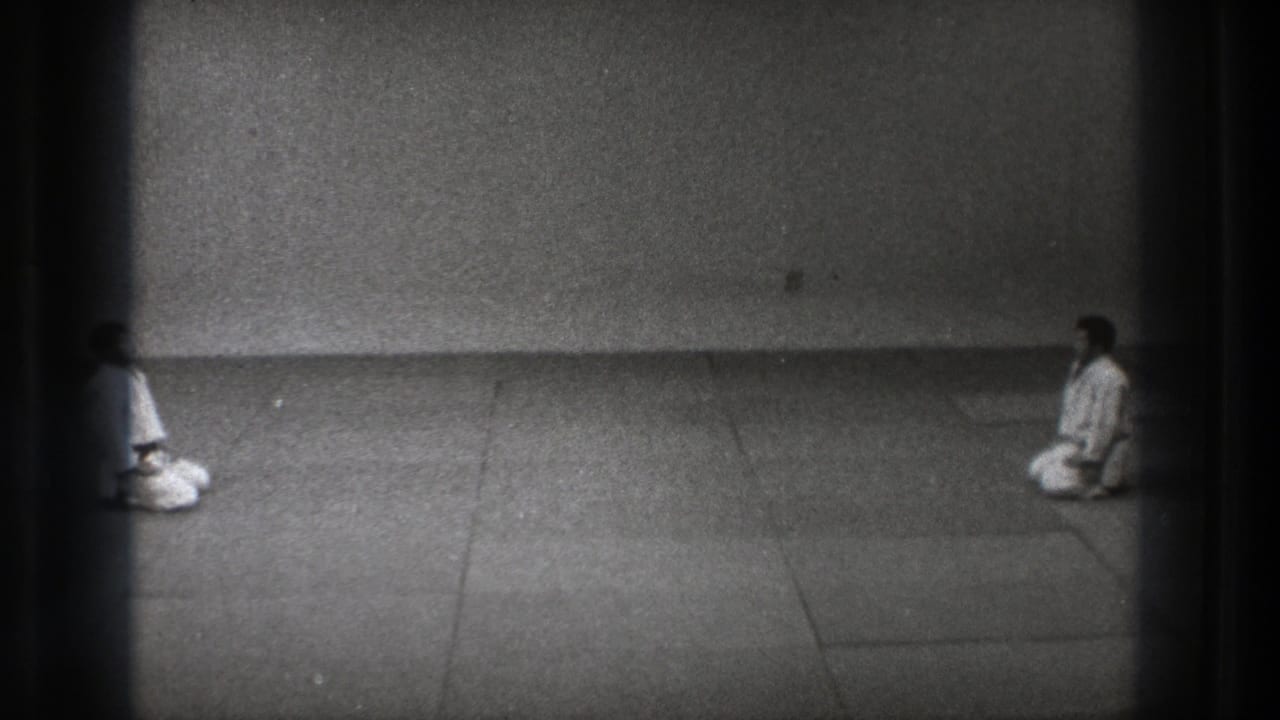1971 Tokyo frame showing two martial arts practitioners seated on their knees across a sparse matted dojo space.