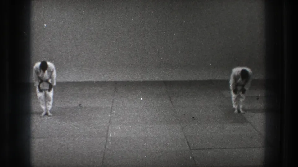 Tokyo 1971 black-and-white 8mm frame showing two karate practitioners bowing before a match on a plain mat area.