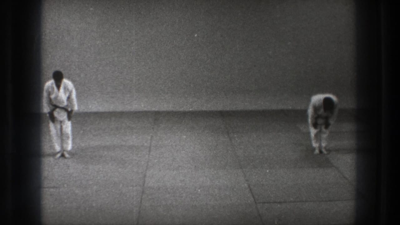 Tokyo 1971 frame with one karate practitioner upright and the other still bowing in a sparse indoor match setting.
