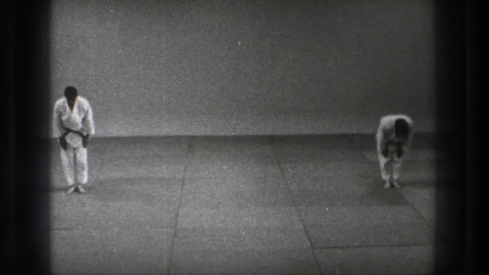 Tokyo 1971 frame with one karate practitioner upright and the other still bowing in a sparse indoor match setting.
