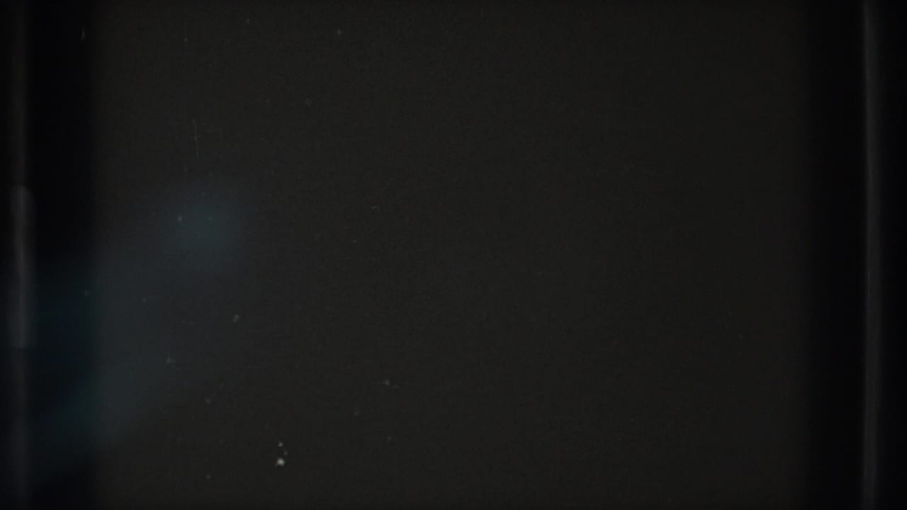 Dark 8mm leader-like frame with faint gray surface texture, scratches, dust, and heavy edge shadowing.