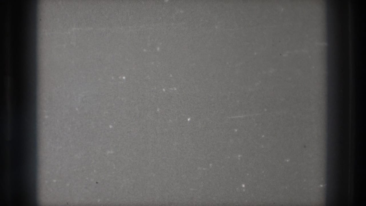 1971 Tokyo 8mm frame of a grey, untuned television-like screen with dark edge bars, grain and small white specks.