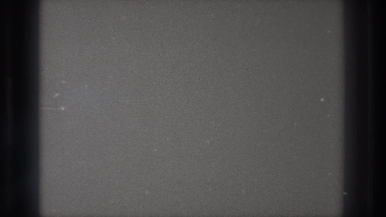 Blank 8mm frame from a Tokyo Japan 1971 source, showing gray film texture, dark edge bands, dust, and faint scratches.