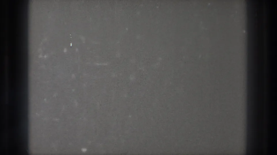 Blank 8mm frame from the 1971 Tokyo source, with a dark vertical band, grain, small white specks, and faint marks.