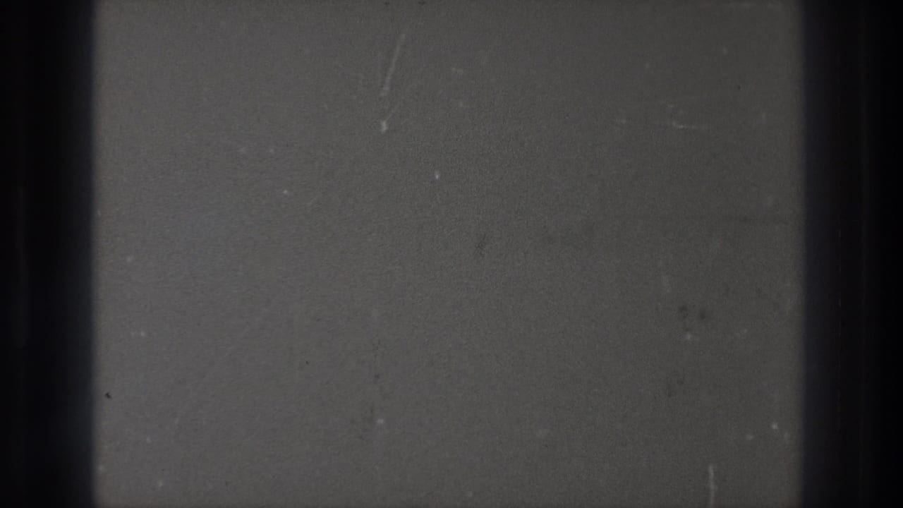 1971 Tokyo 8mm footage showing a close view of film passing through projection, with gray frame areas, dark bars, dust, and scratches.