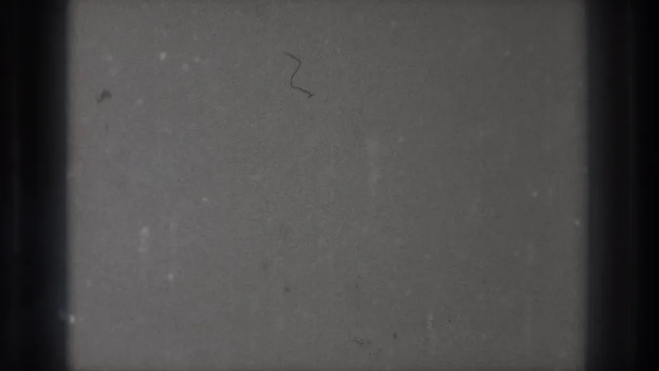 Blank 8mm frame from the Tokyo 1971 reel, showing gray emulsion, gate-edge shadows, dust, and a small curved scratch.