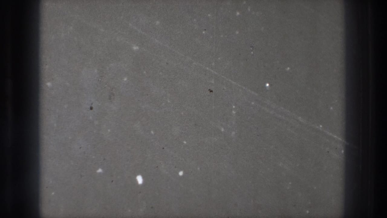 1971 Tokyo 8mm frame showing a dark gray field with dust specks, scratches, and heavy vertical edge shadows.