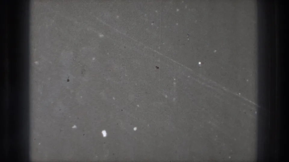 1971 Tokyo 8mm frame showing a dark gray field with dust specks, scratches, and heavy vertical edge shadows.