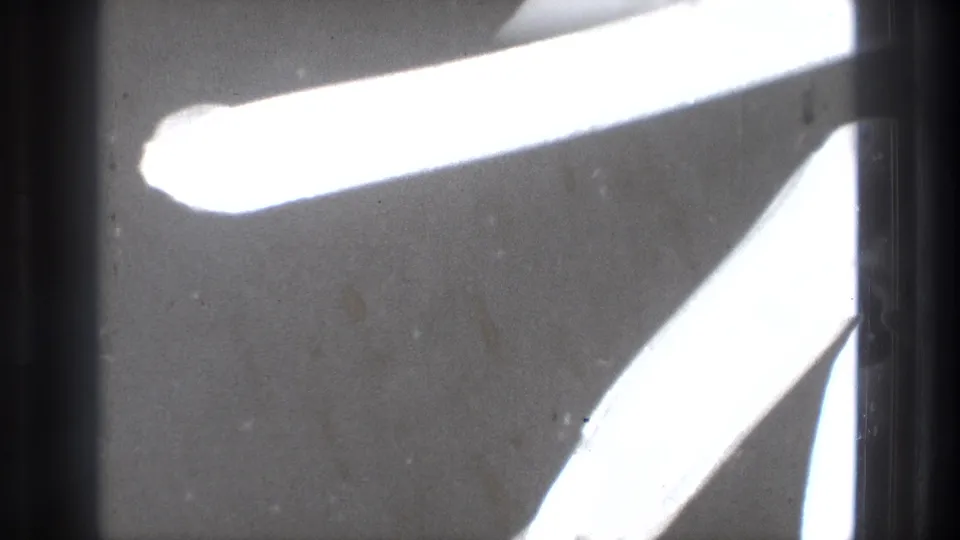 1971 Tokyo 8mm frame with bright elongated light forms cutting across a dark, grainy surface.