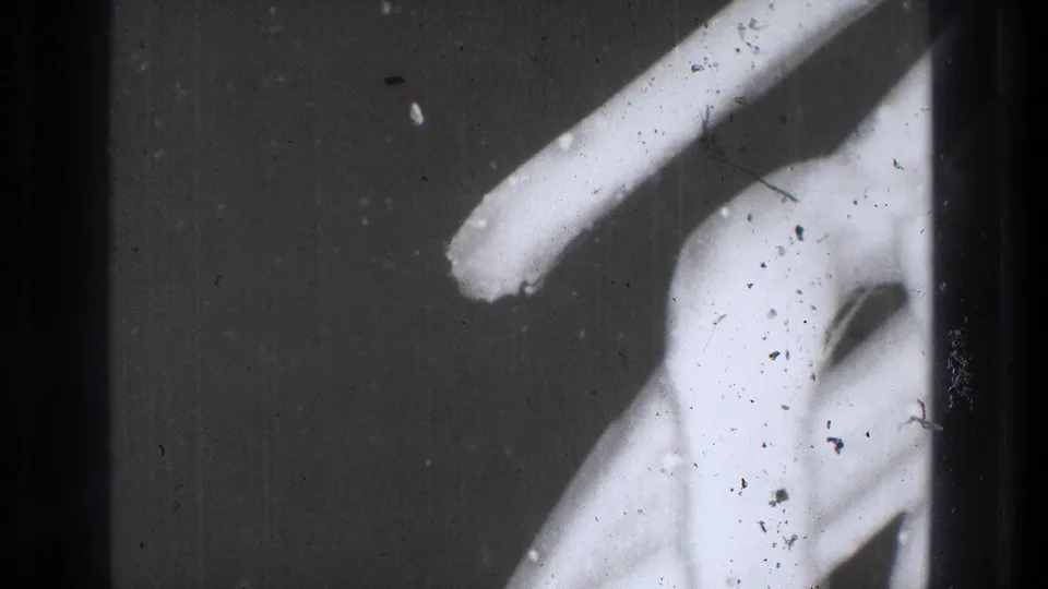 1971 Tokyo 8mm frame showing a diagonal white light streak, pale abstract form, dust, and scratches.
