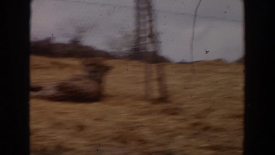 1974 Irvine 8mm frame begins with a blurred view across dry straw and fencing, framed by dark vertical edges.