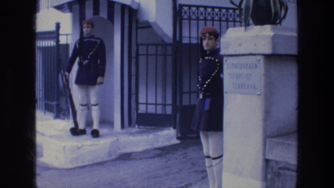 Two uniformed guards stand near a white guardhouse gate.