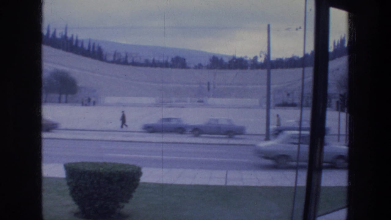Cars move along a broad street behind a window frame, with a pedestrian in the distance.