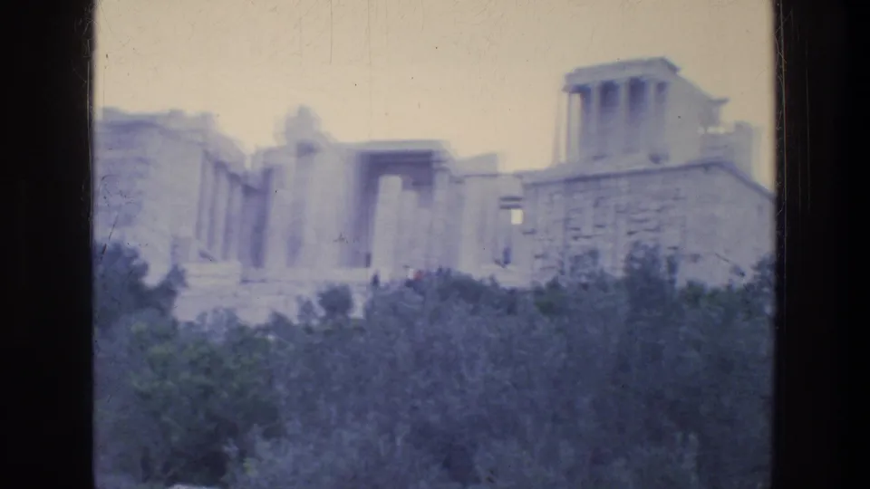 1976 Athens home-movie frame showing classical ruins and a raised stone wall partly obscured by trees.