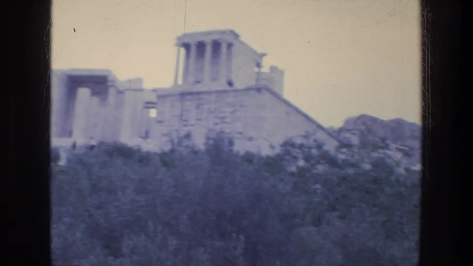8mm frame from Athens in 1976 showing a temple-like columned section and stone wall beyond trees.