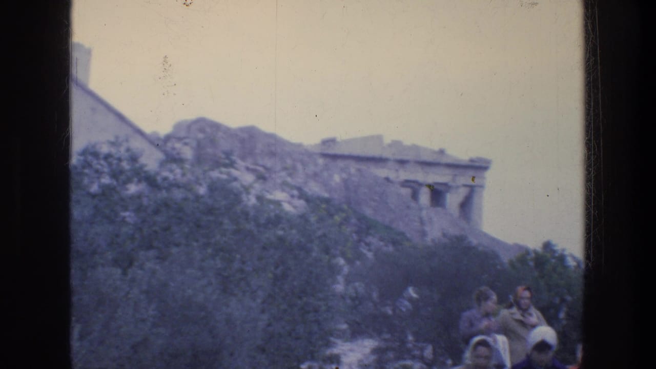 Acropolis hill with Parthenon partly visible and tourists standing on a rocky path.