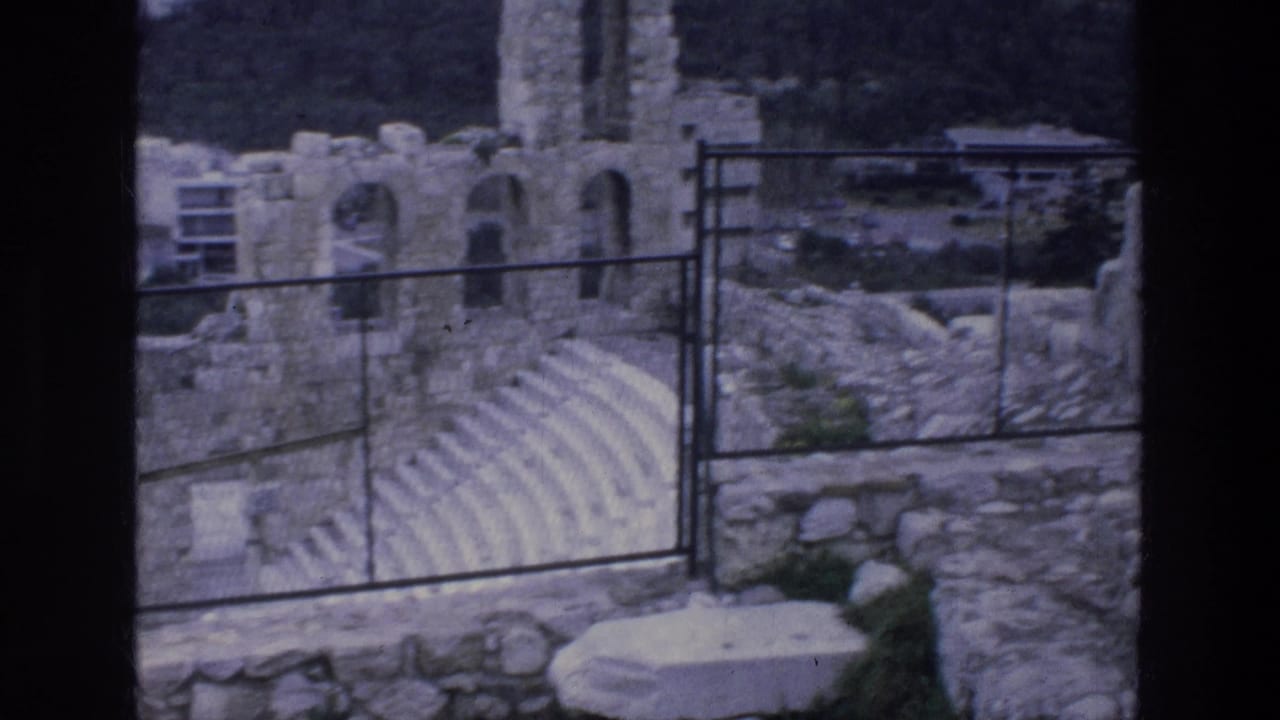Stone amphitheater seating and arched ruins behind a metal railing.