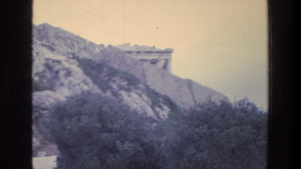 Rocky hillside with pale stone ruins and trees in the foreground.