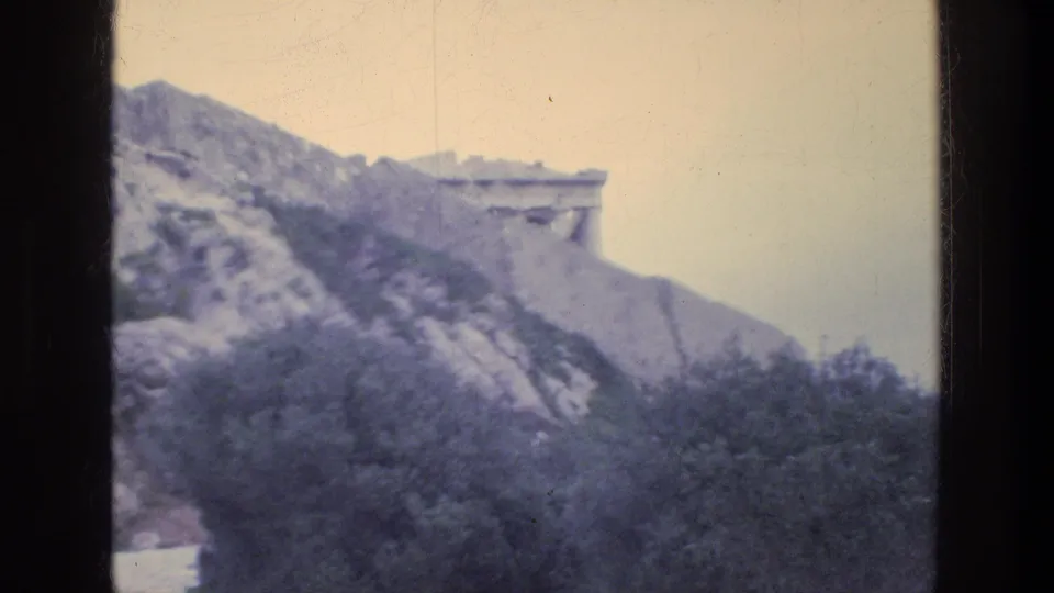 1976 Athens view across a rocky hillside toward pale stone structures, with shrubs and trees below.