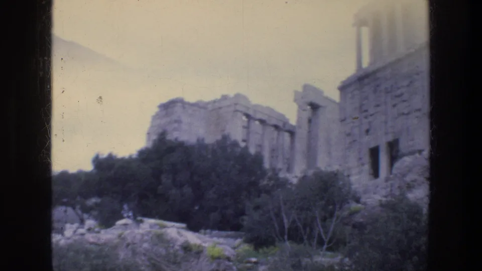 1976 Athens visitor-shot frame of columned stone ruins, rough masonry, trees, and rocky ground.