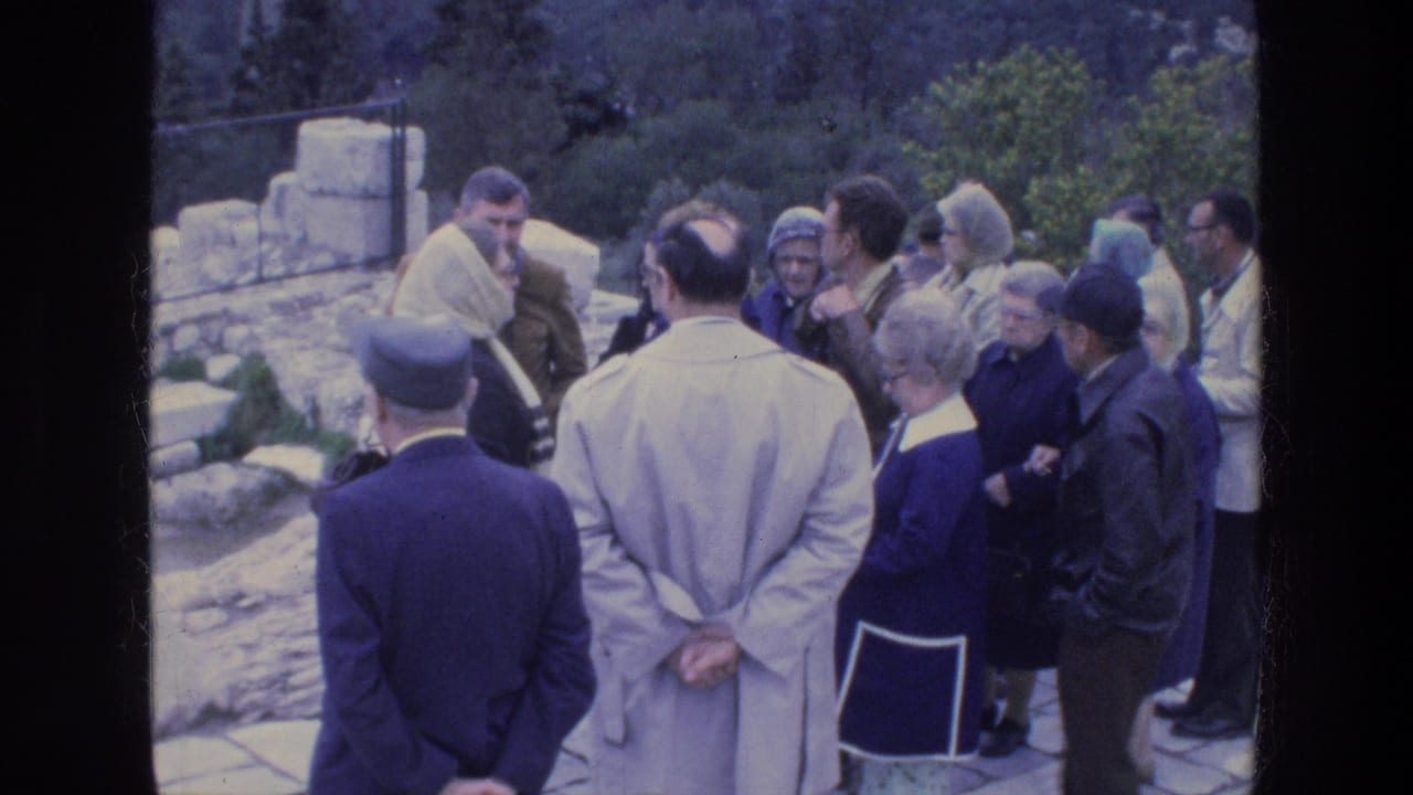 Adult tourists in coats and hats gather on a stone terrace in Athens, appearing to listen during a guided site visit.
