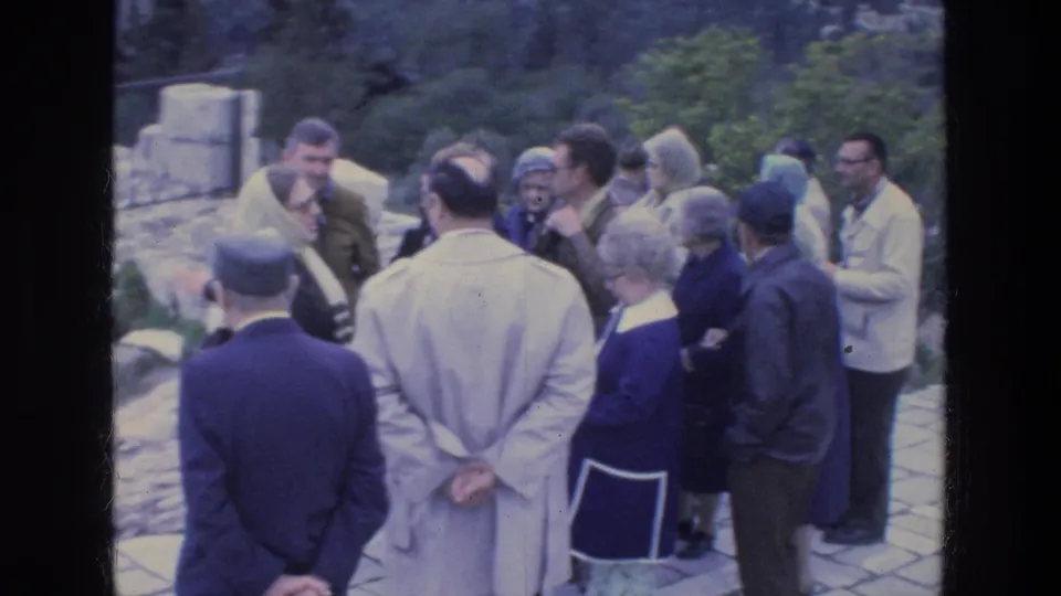 1970s Athens travel footage shows adults in coats, hats, and scarves gathered closely during a guided ruins visit.