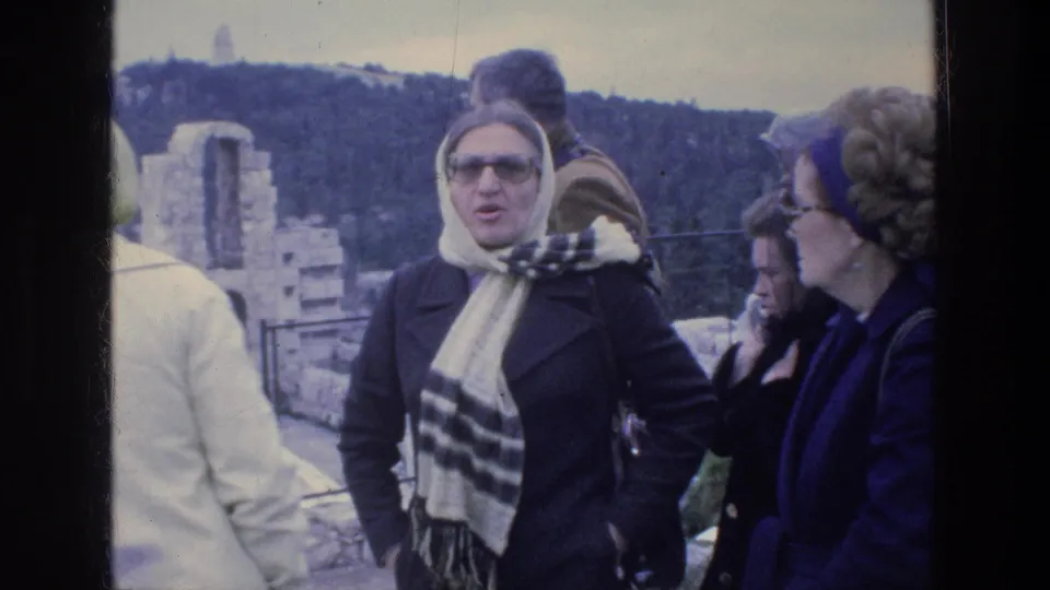 1976 Athens home-movie frame of adult tourists near ancient stone ruins, with headscarves, coats, and sunglasses visible.