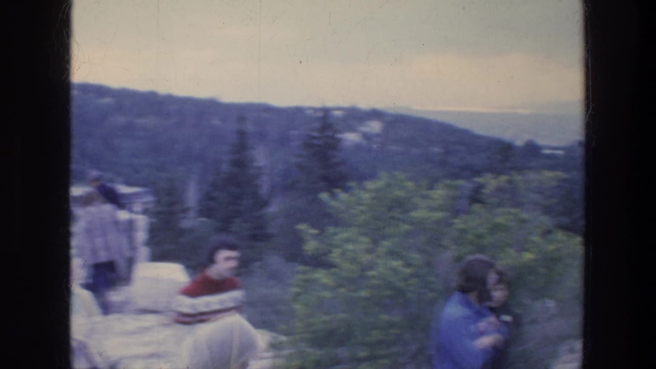 Tourists on a hilltop path with trees, distant buildings, hills, and a hazy sky.
