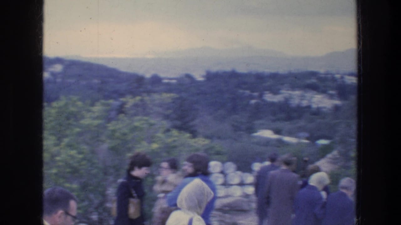 Visitors walking along a path above green hills and distant buildings.
