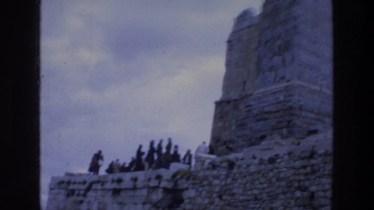 Tourists walk along stone walls beside large ruins at the Acropolis.