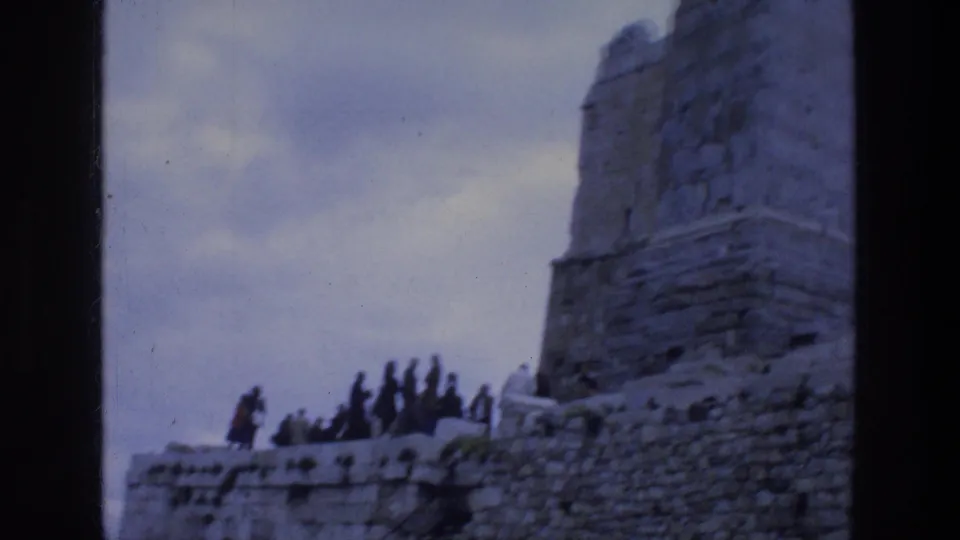 1976 8mm view of tourists moving along stonework near the Acropolis ruins in Athens under a pale sky.