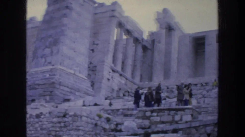 1976 home-movie frame of tourists on steps among Acropolis ruins, with soft focus and faded color.