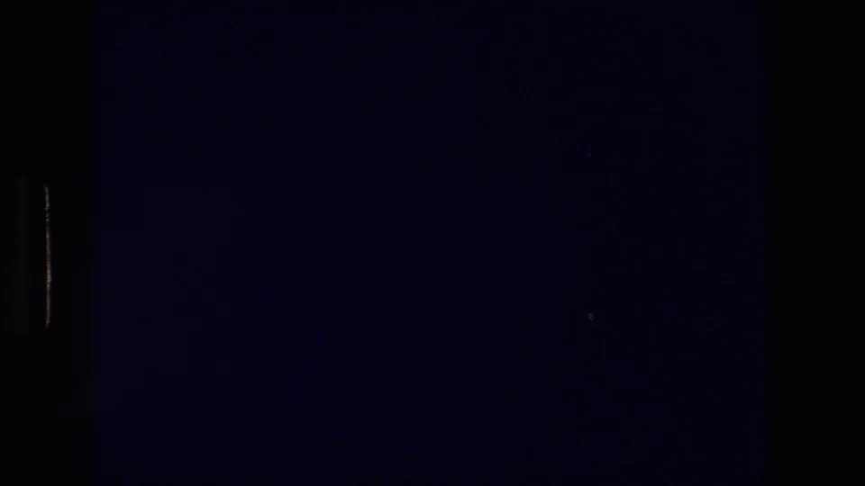 Underexposed 8mm frame at the start of the Athens travel clip, with mostly dark film area and only faint detail visible.