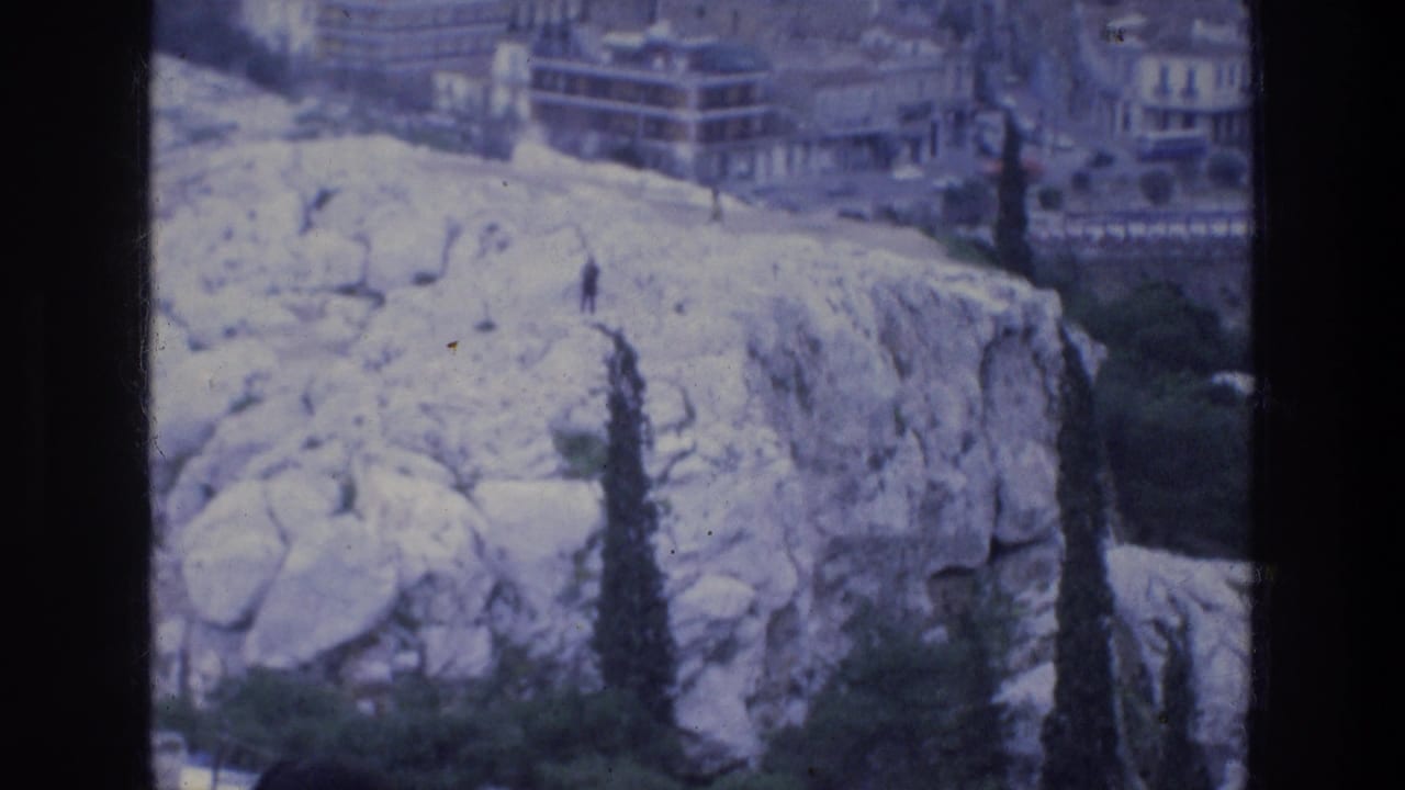 1976 8mm view of pale rocky ground near the Acropolis area with Athens buildings and trees beyond.