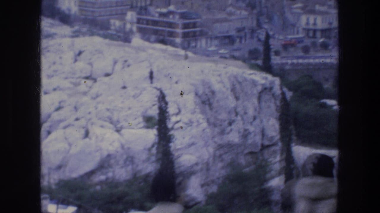 Rocky overlook and city buildings with a partial person at the frame edge.