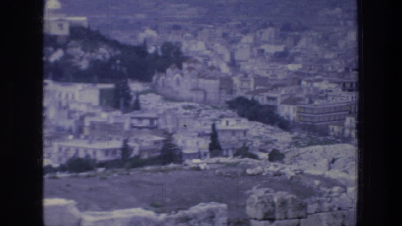 1976 8mm view over Athens buildings, rocky hillside, trees, and pale ruin-like stonework in soft blue-tinted focus.