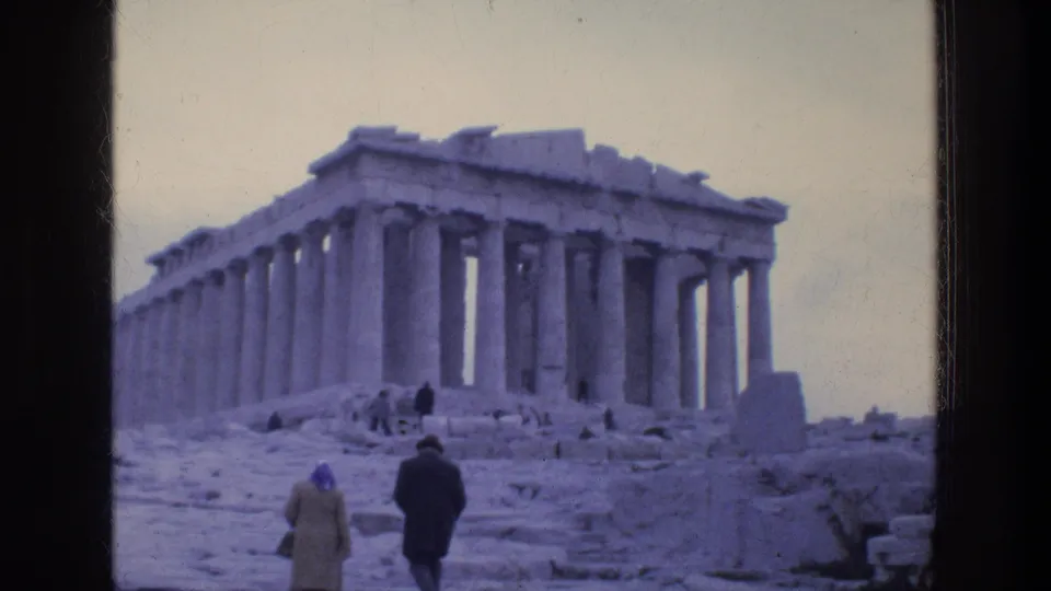 1976 Athens frame showing the Parthenon from below, with visitors moving through the ruins and soft blue-purple 8mm color.