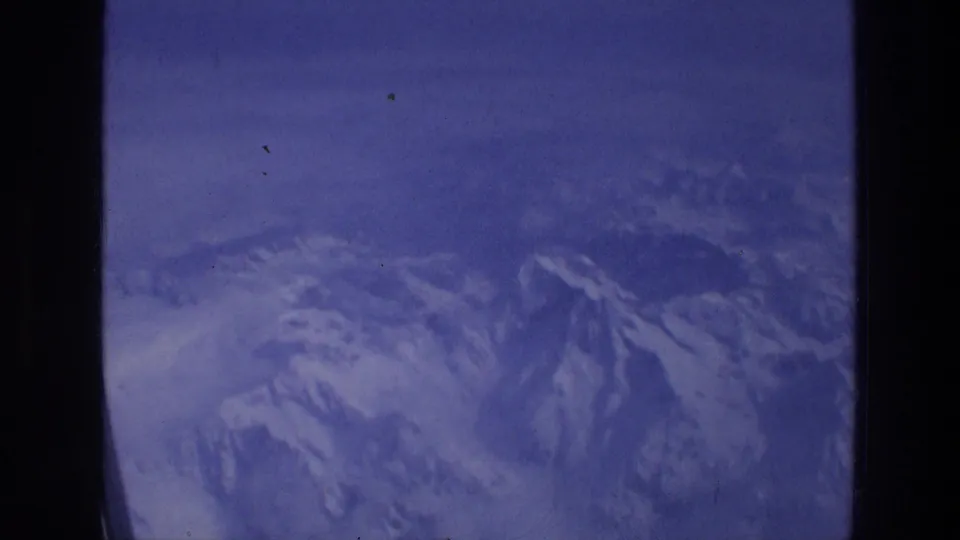 Aerial 8mm frame from an airplane window showing hazy snow-covered mountain peaks below, likely part of the same 1976 travel reel.