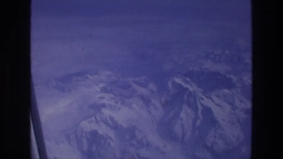 Aerial mountain view from a plane, with snow on the ridges and visible 8mm film grain from the 1976 Greece travel reel.