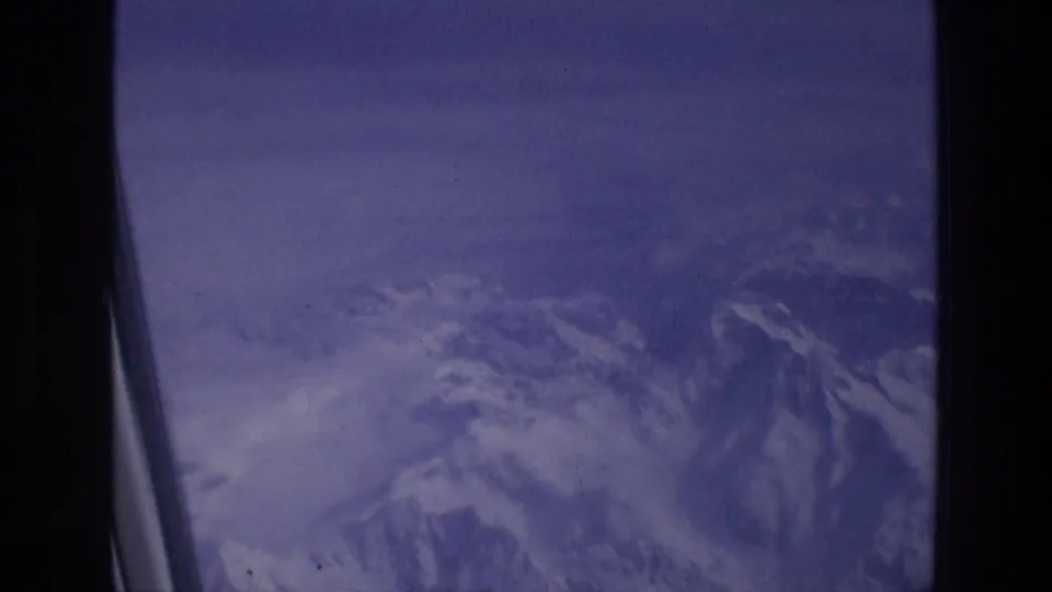 1976 8mm travel frame showing snow-covered mountains through an aircraft window in the Athens, Greece travel context.