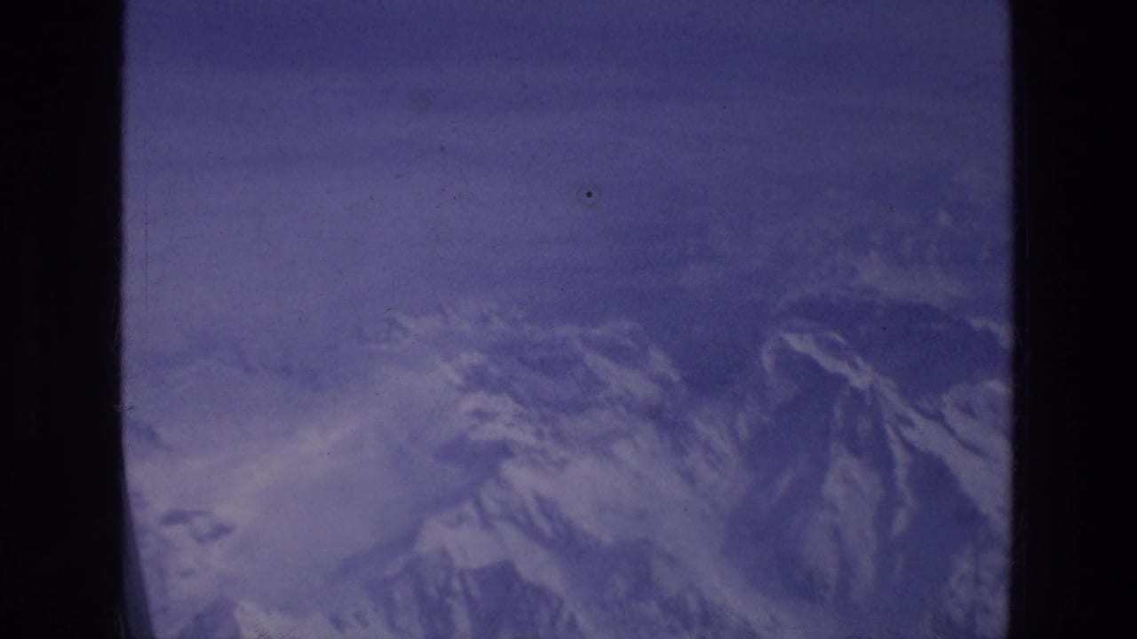 Aerial view of snow-streaked mountains framed by dark airplane window posts.