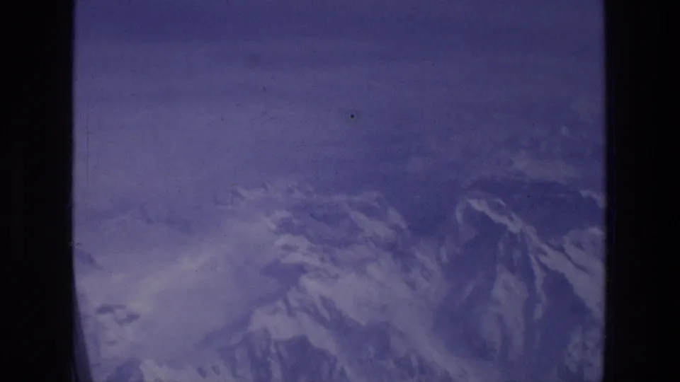 Snowy mountain ridges are viewed from a plane window in this 1976 8mm Greece travel shot.