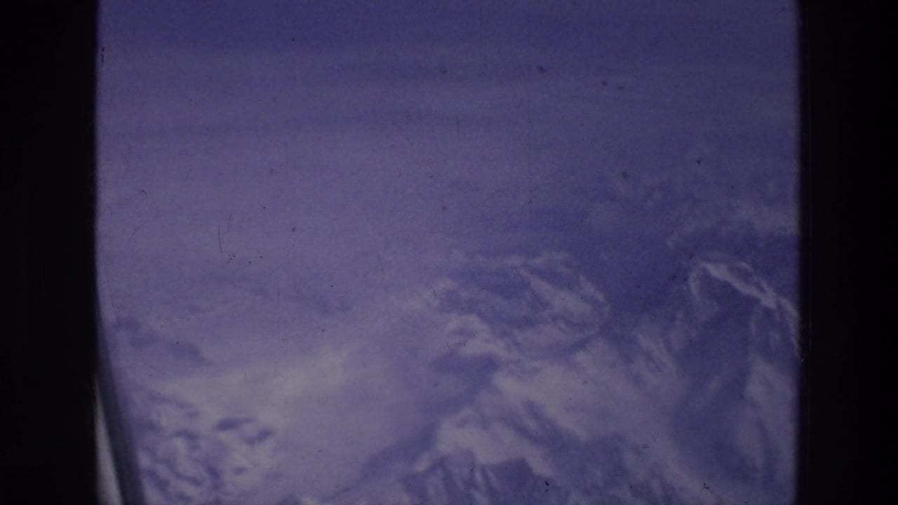 Airplane window view of snowy mountain terrain below.