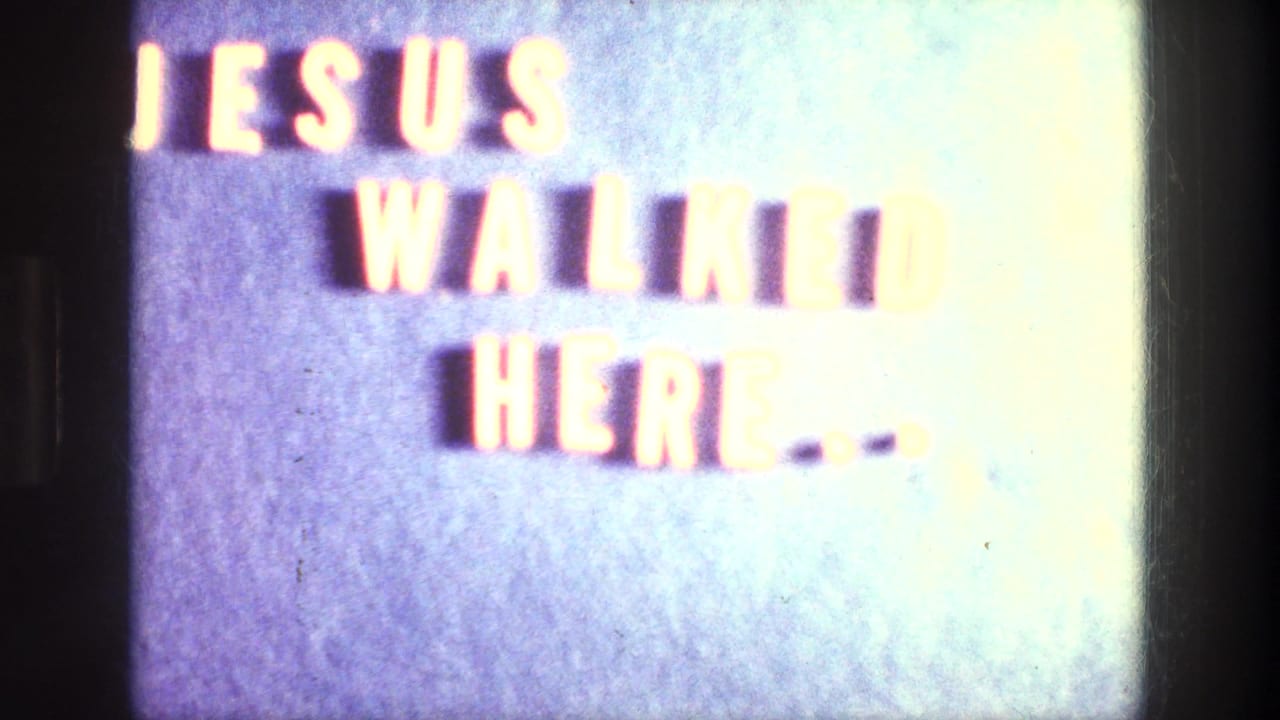 Overexposed close-up of a sign reading Jesus walked here on a blue wall.
