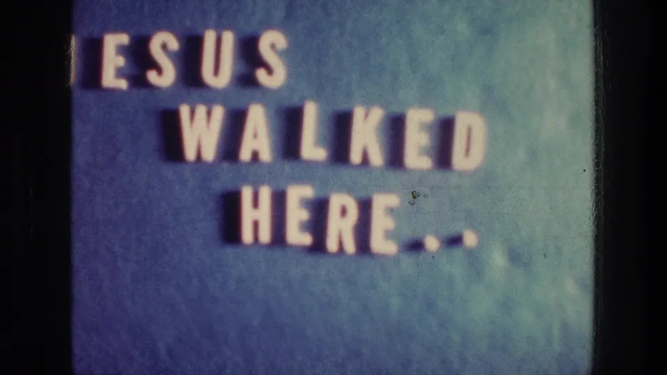 1976 Athens 8mm frame showing the religious sign partly cropped, with white letters and shadows on a blue wall.